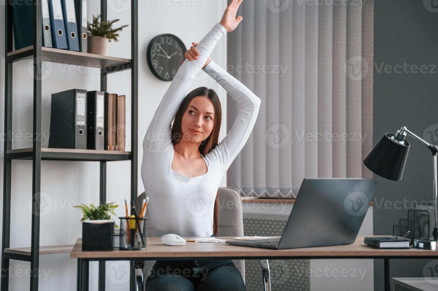 Doing exercise, break. Young beautiful woman in white clothes is in the office photo