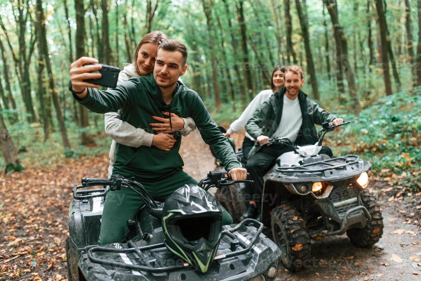 Making ,a selfie by smartphone. Two couples on a quad bike in the forest during the day photo