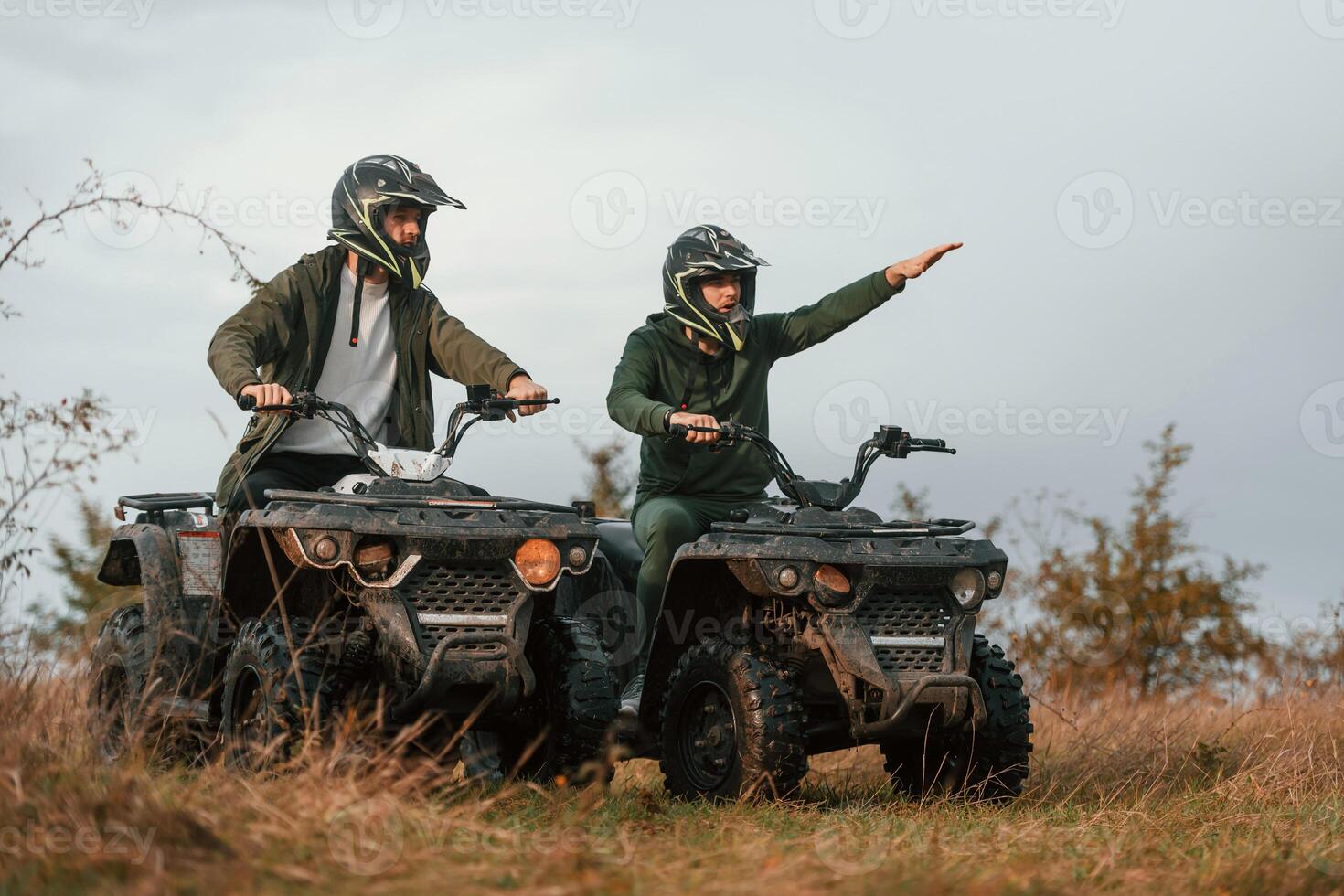 Showing the path by a hand. Two men are on the quad bikes outdoors on the field photo