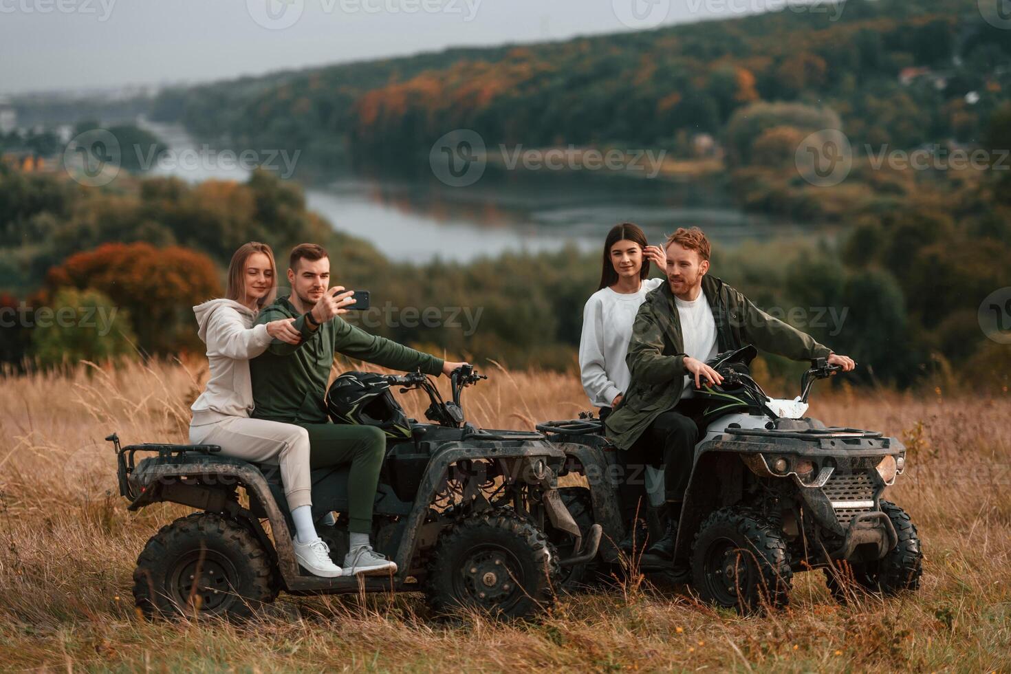 Making a selfie by smartphone. Two young couples with quad bikes is together on the field. photo