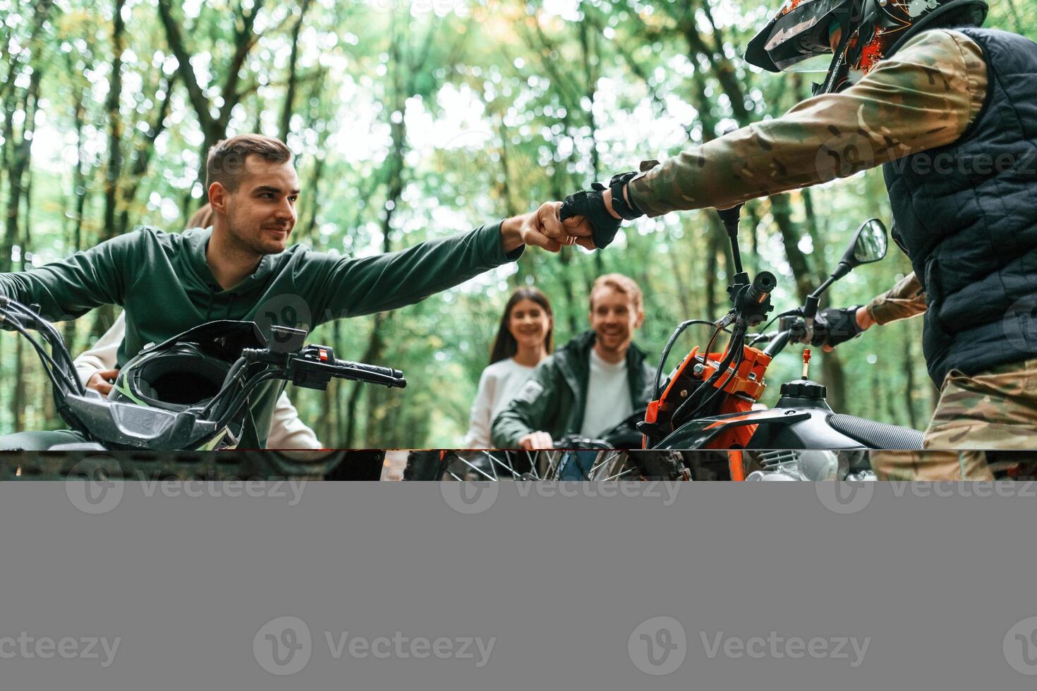 Knocking fists, gesture. Two couples on ATV with man that is on the bike in the forest. photo
