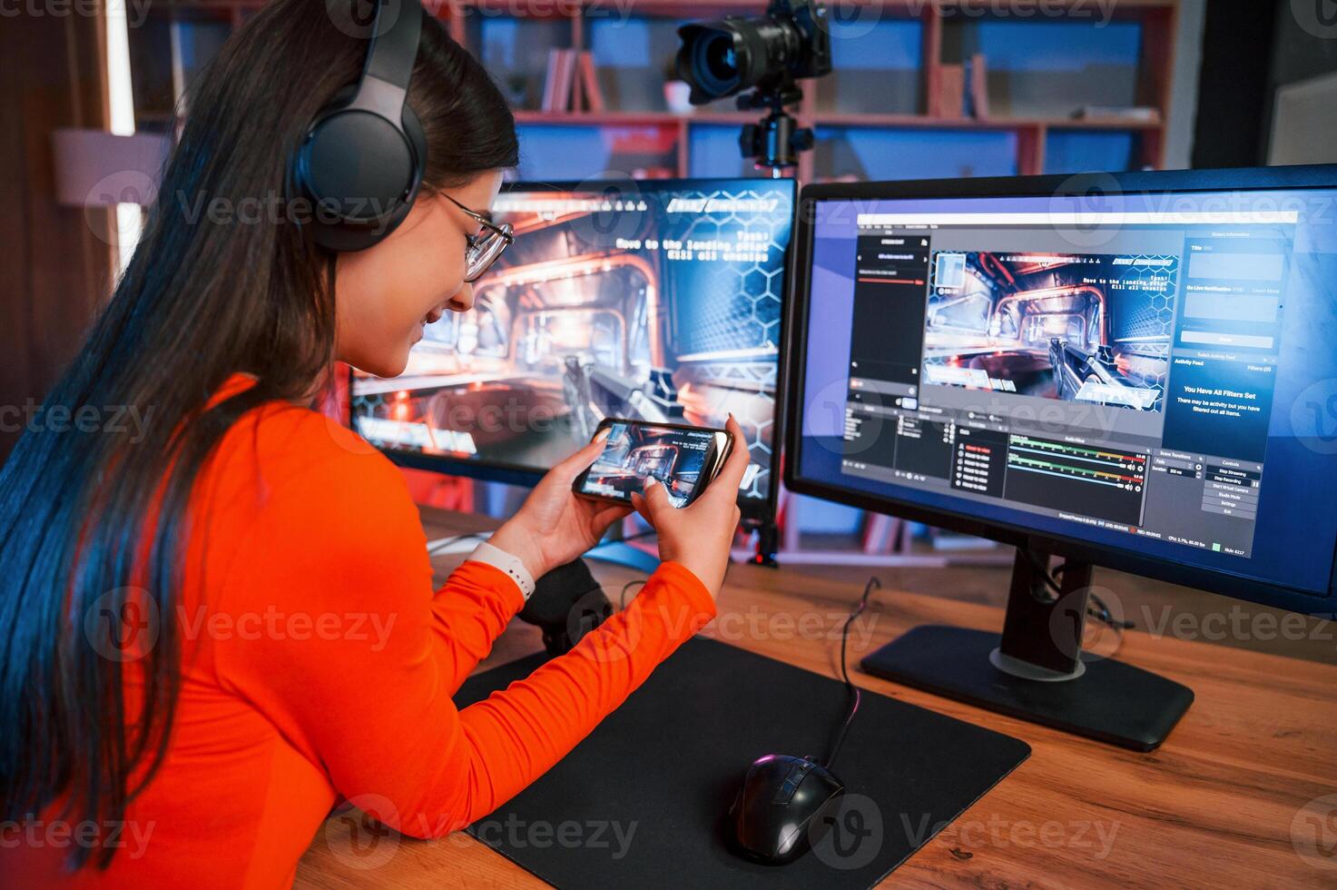 Holding smartphone in hands. Conception ,of victory. Young beautiful game streamer is indoors with pc photo