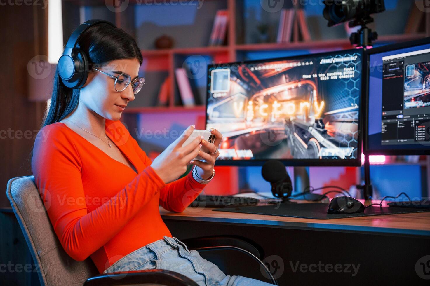 Holding smartphone, in hands. Conception of victory. Young beautiful game streamer is indoors with pc photo