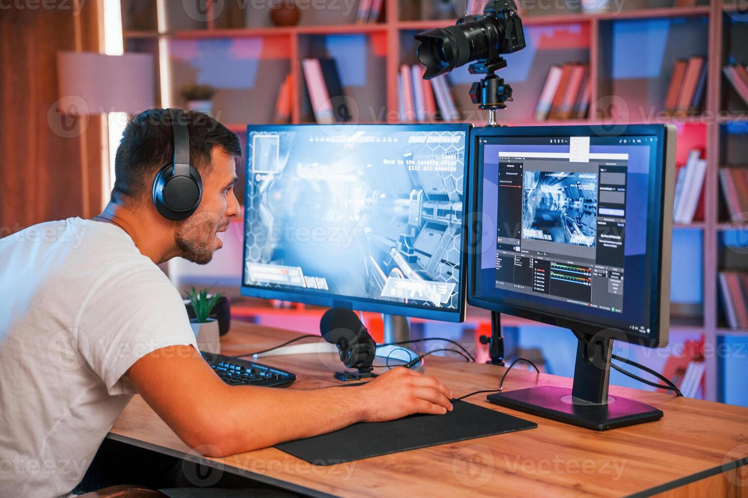 Playing ,first person shooting game. Male streamer in casual clothes is indoors with pc photo