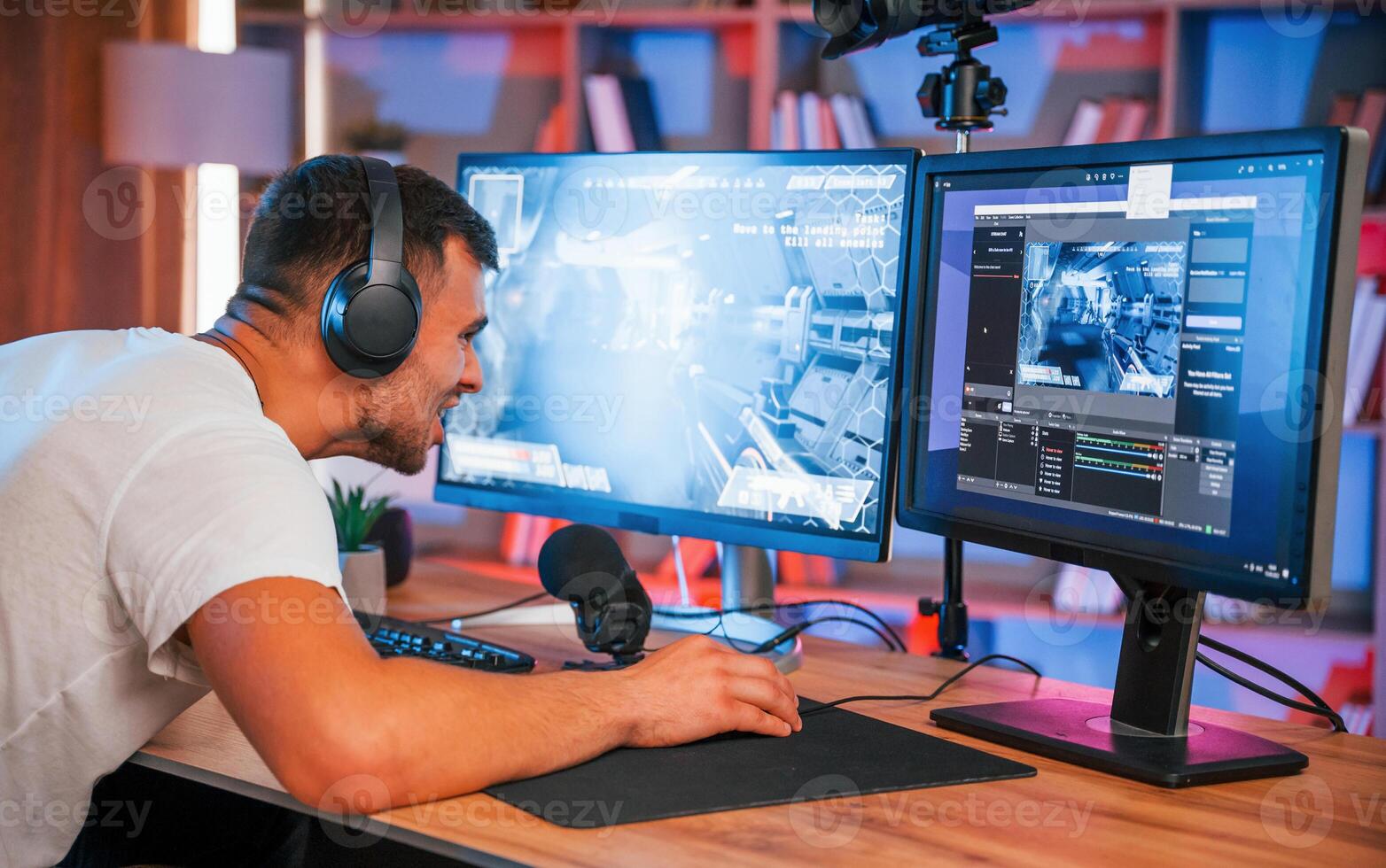 Playing, first person shooting game. .Male streamer in casual clothes is indoors with pc photo