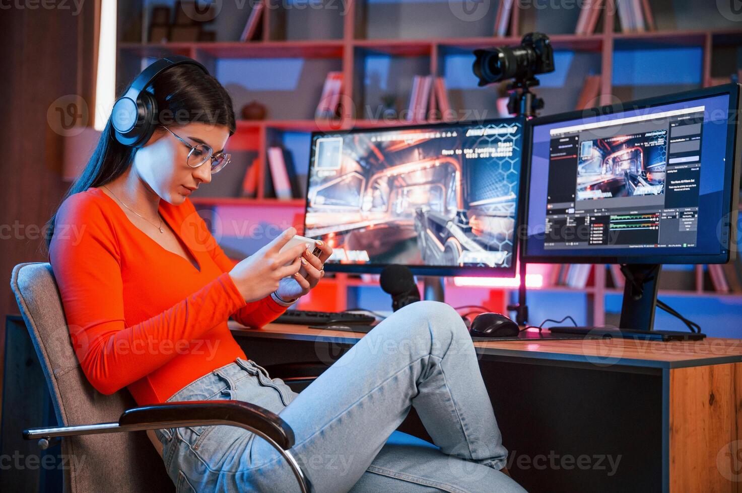Holding smartphone in hands. Conception of victory. Young beautiful game streamer is indoors with pc photo