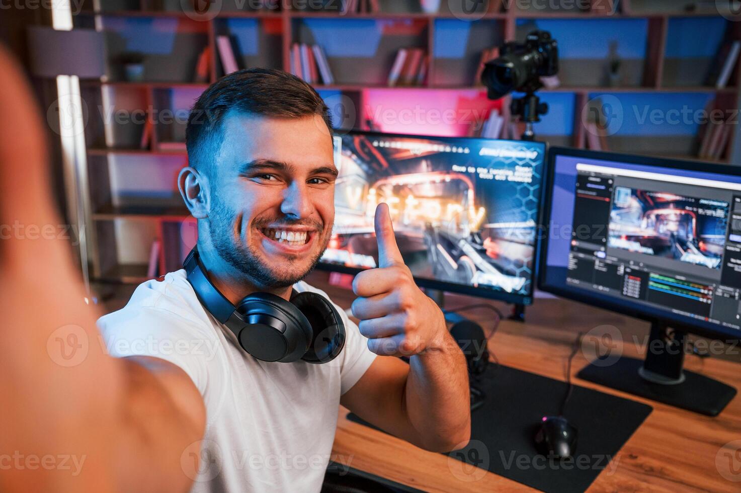 Making selfie, celebrating victory. Male ,game streamer in casual clothes is indoors with pc photo