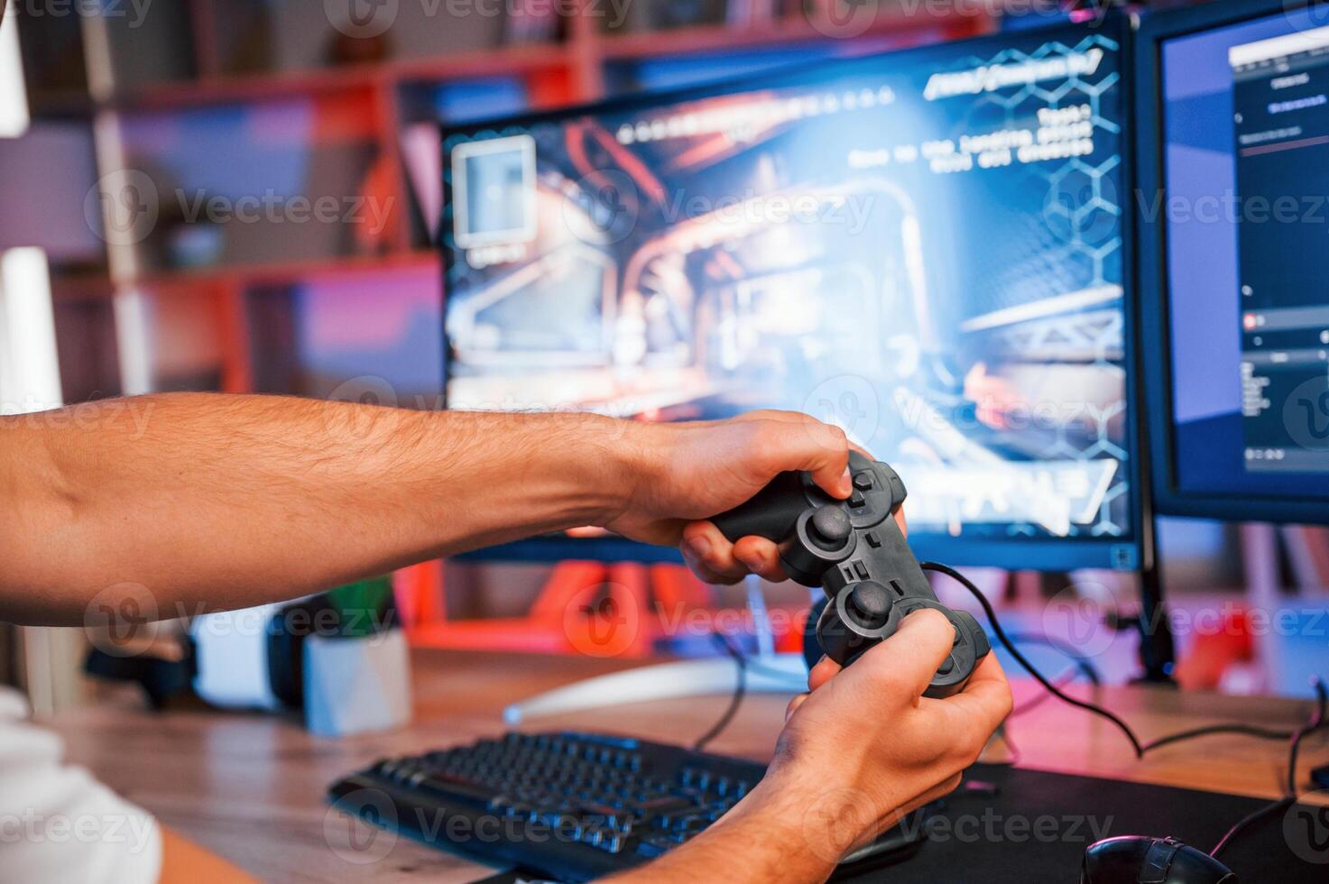 Close up view of hands with, joystick controller. Male game streamer in casual clothes is indoors with pc photo
