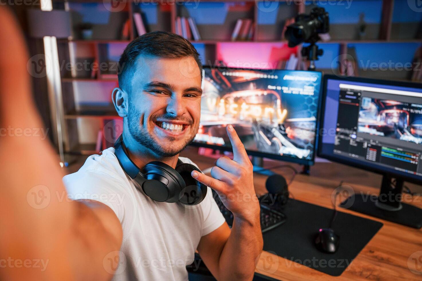 Making, selfie, celebrating victory. Male game streamer in casual clothes is indoors with pc photo