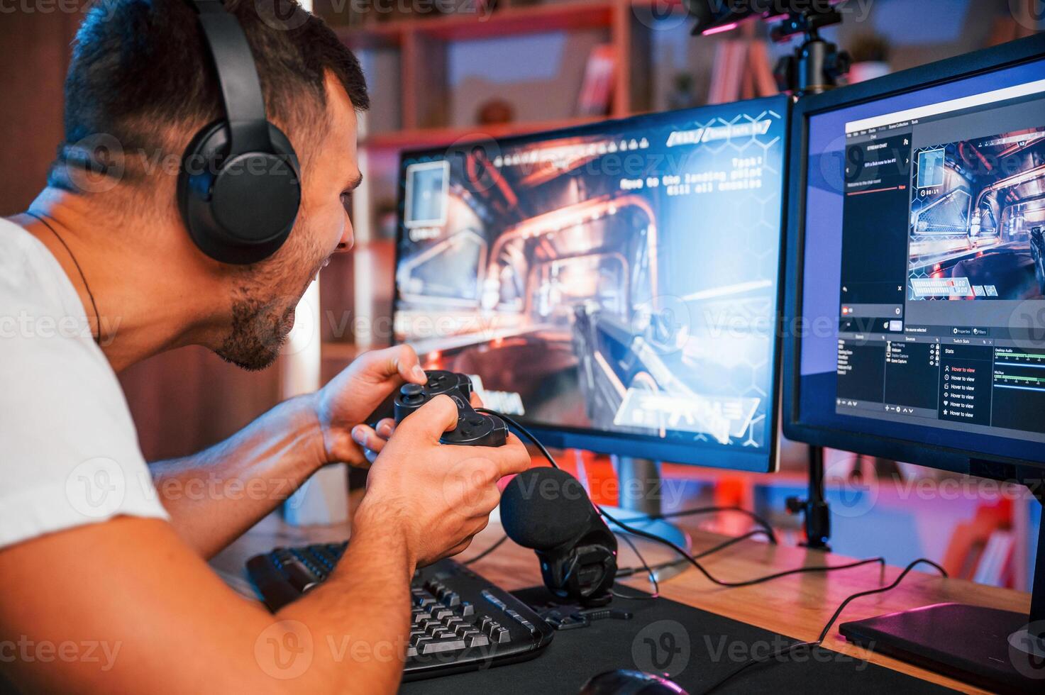 Playing first person shooting game. Male streamer in casual clothes is indoors with pc photo