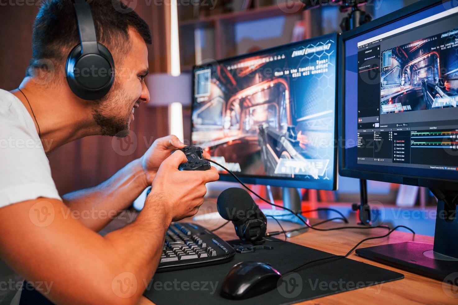 Playing first person shooting game.. Male streamer in casual clothes is indoors with pc photo