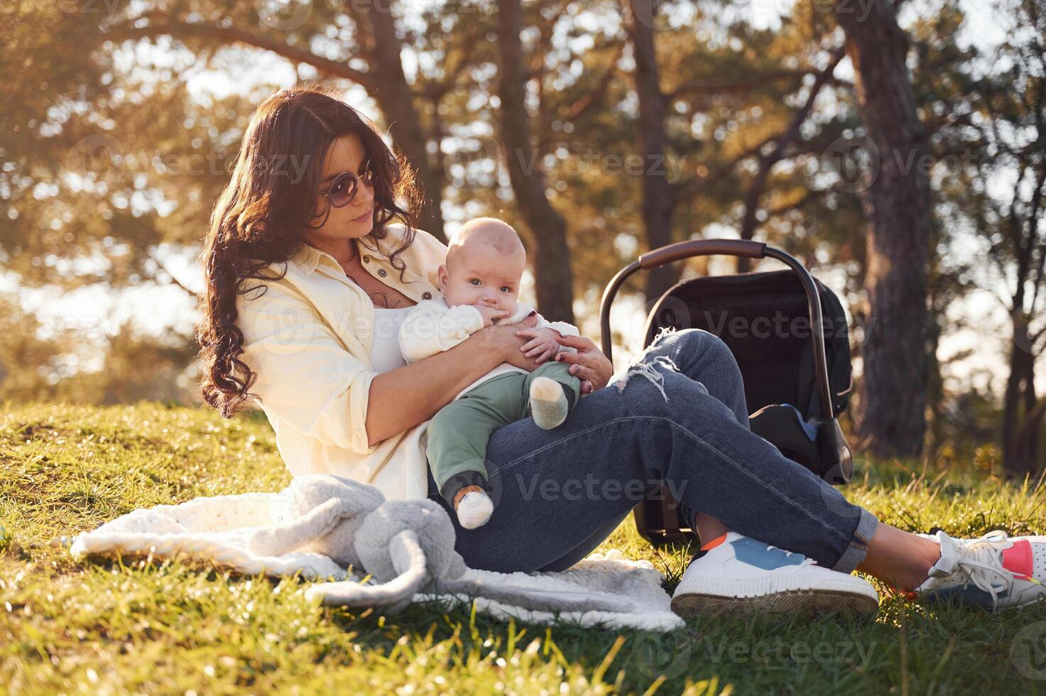 Sitting, on the ground. Beautiful mother with her little son is outdoors in the forest photo
