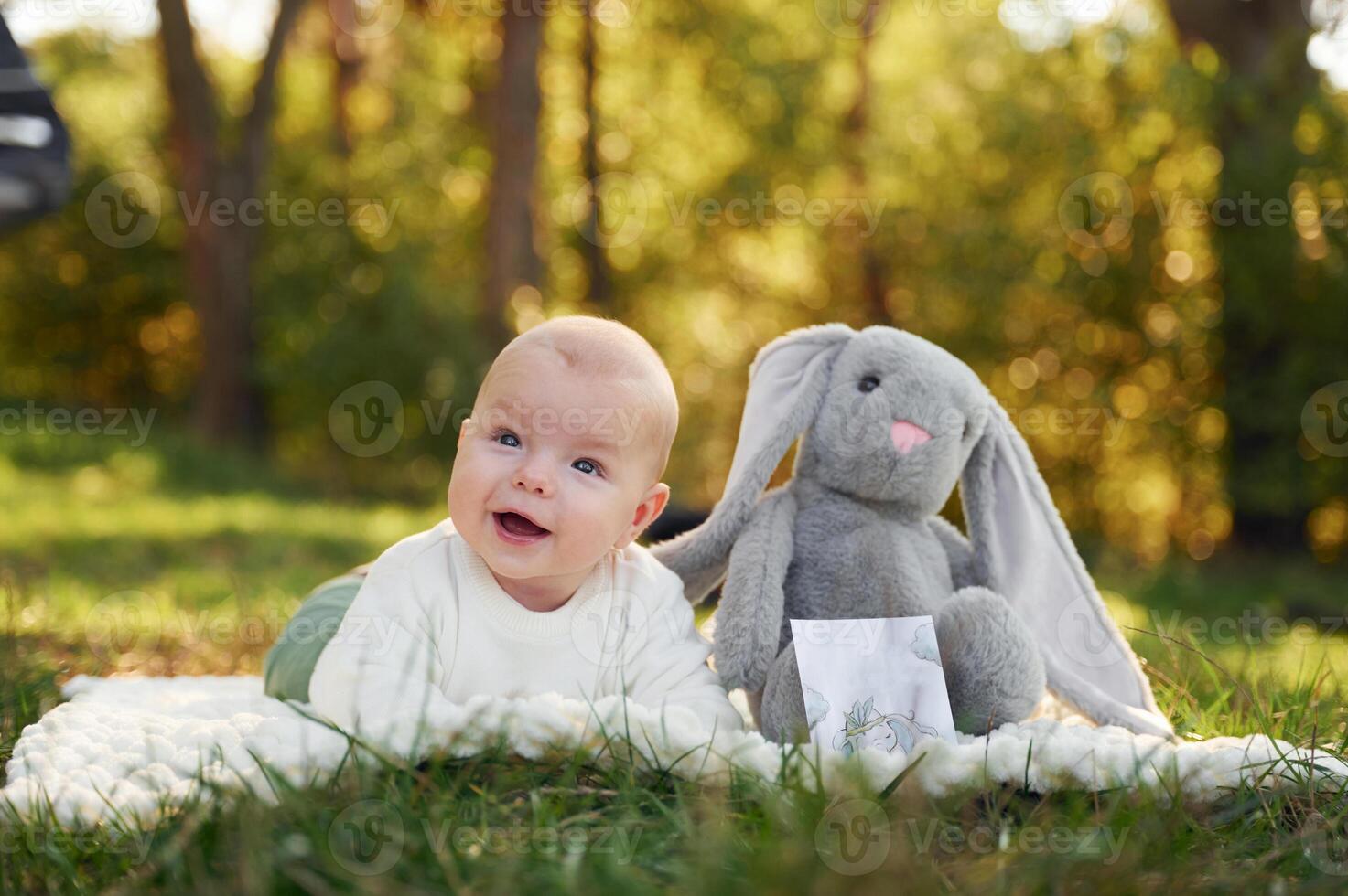 Cute, little baby is laying down on the ground in the forest with toy near him photo