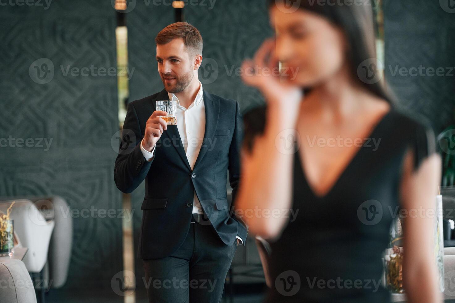 Crying, having conflict. Man in black suit and with drink in hands looks at woman in dress photo