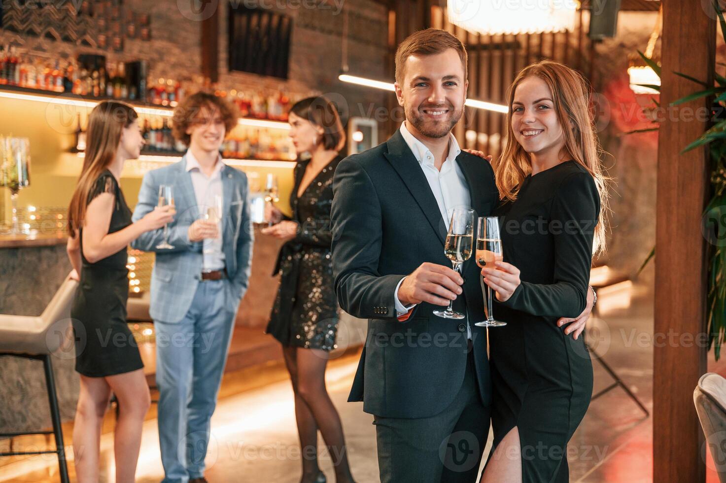 Man with, his woman is standing ,and smiling. Group of people in beautiful elegant clothes are celebrating New Year indoors together photo