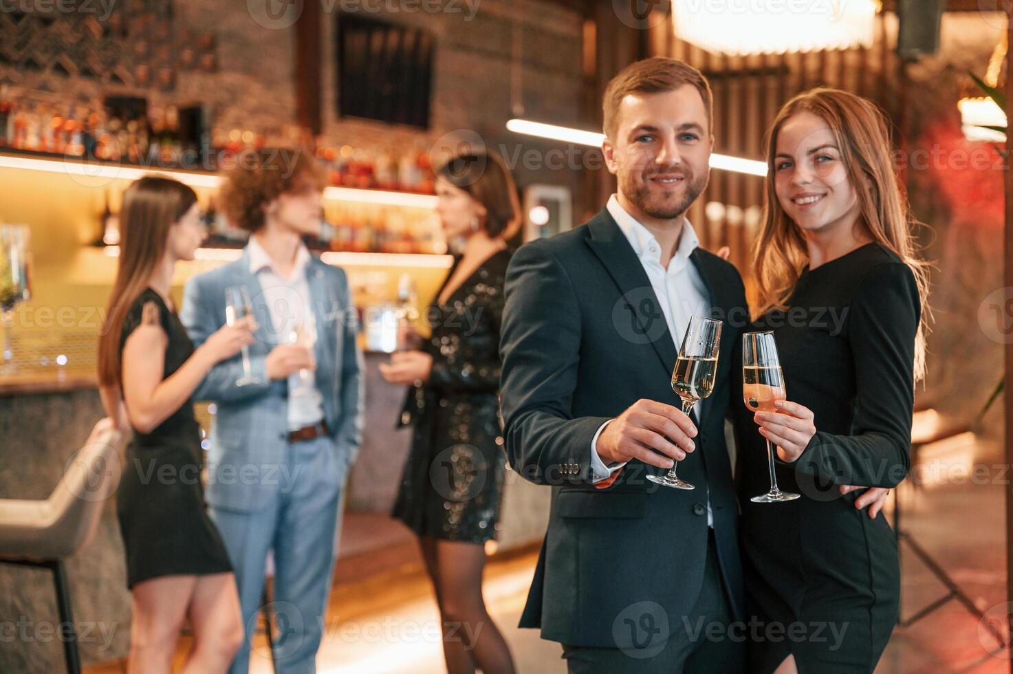 Man with, his woman ,is standing and smiling. Group of people in beautiful elegant clothes are celebrating New Year indoors together photo