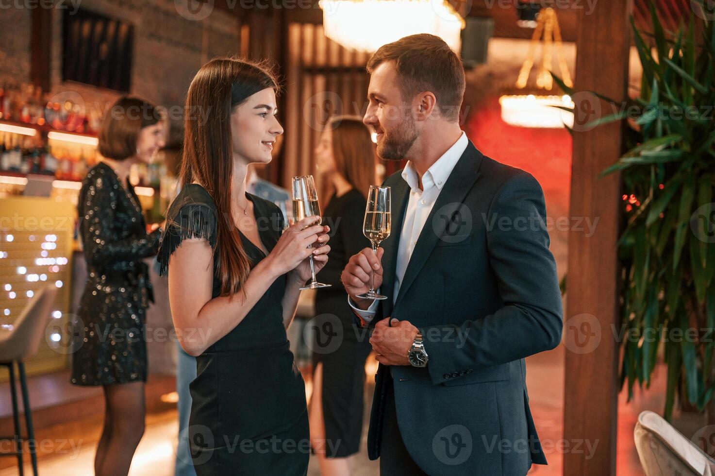 Man with, woman is posing. Group of people in beautiful elegant clothes are celebrating New Year indoors together photo