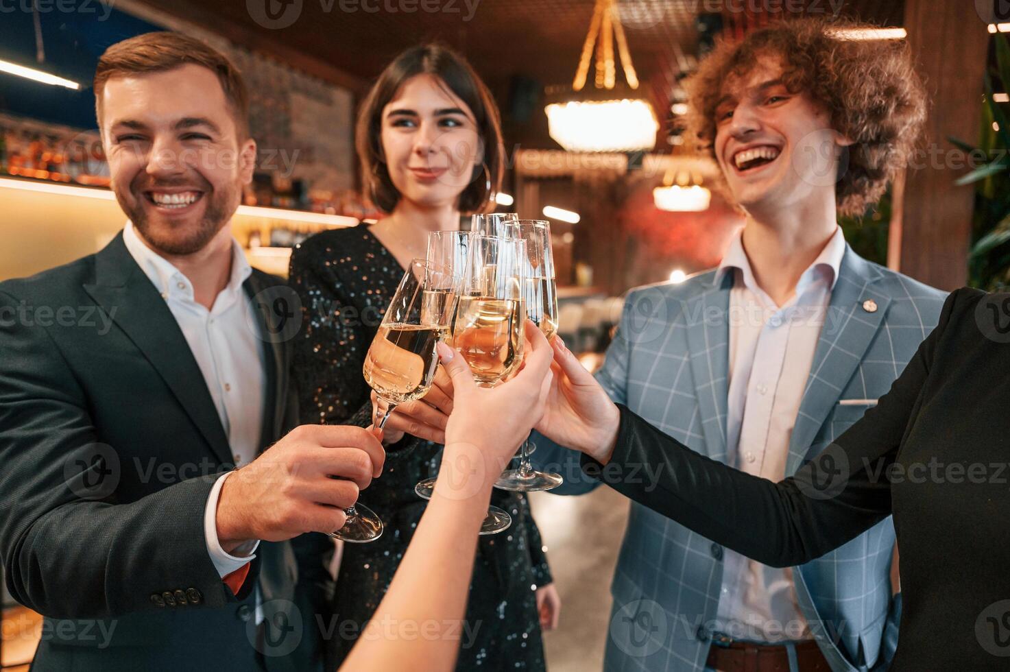 Knocking glasses.. Group of people in beautiful elegant clothes are celebrating New Year indoors together photo