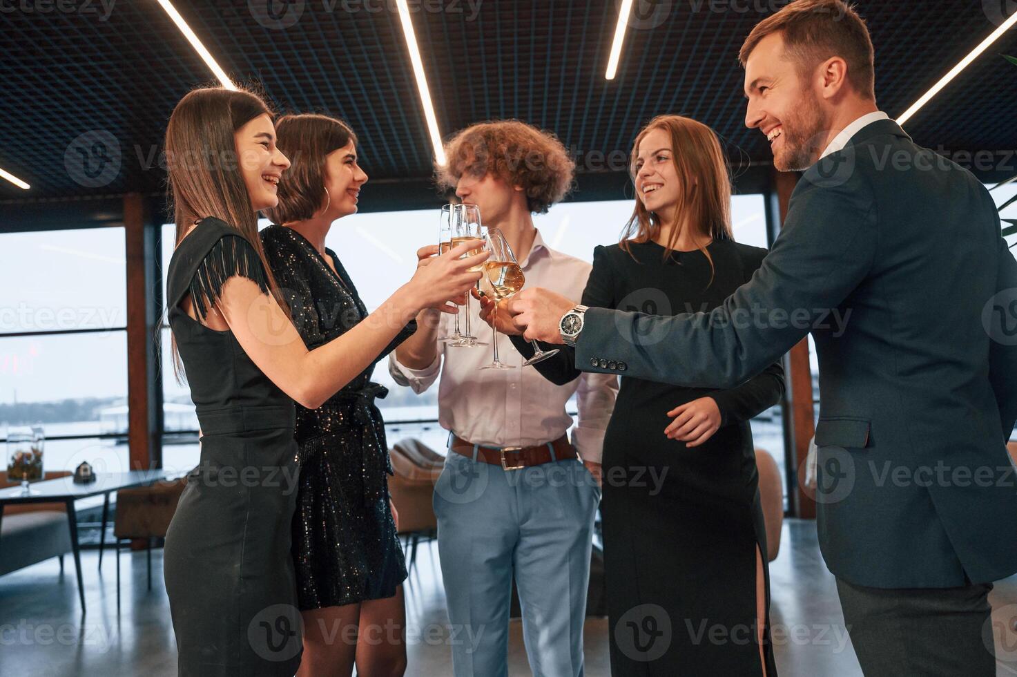 Standing ,and holding ,glasses. Group of people in beautiful elegant clothes are celebrating New Year indoors together photo