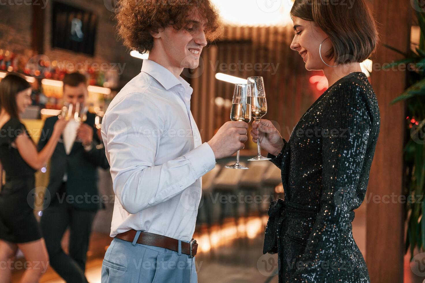 Man,with woman is standing and posing. Group of people in beautiful elegant clothes are celebrating New Year indoors together photo