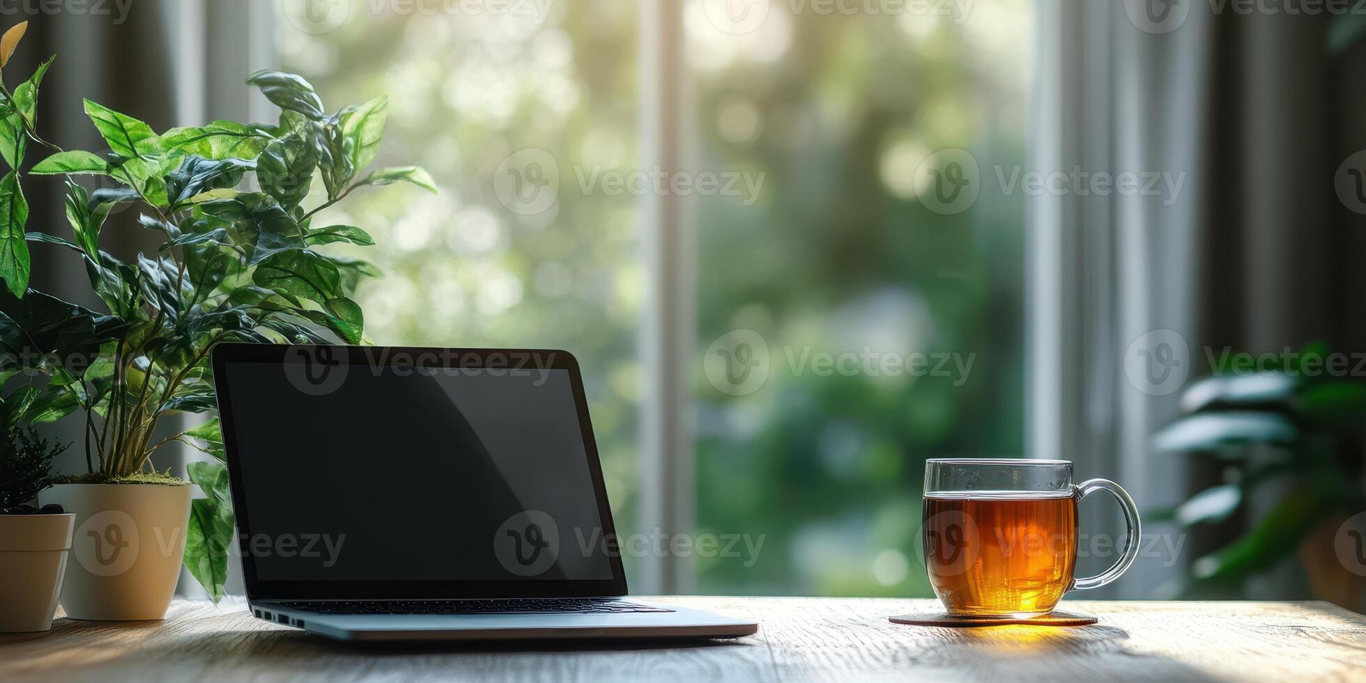 Cozy workspace with laptop and tea by window in bright, green environment during afternoon sun photo