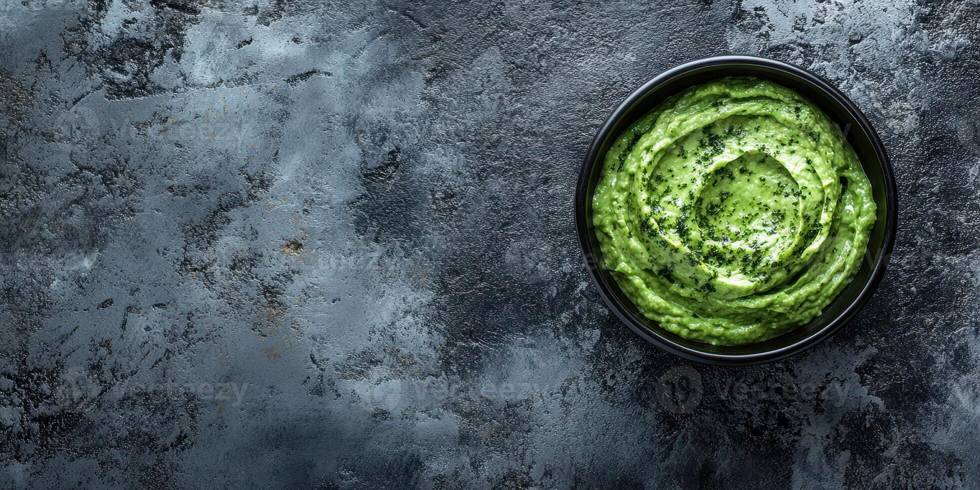 Fresh green dip served in a black bowl on a textured dark surface enhancing the vibrant color of the ingredients photo
