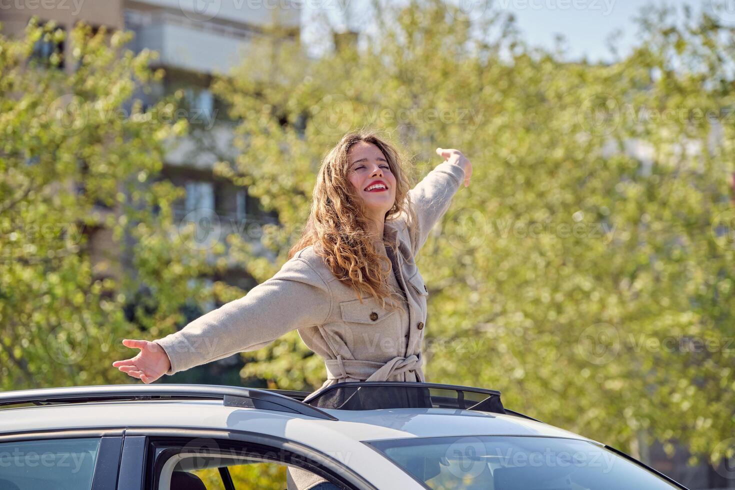 Smiling woman standing in car sunroof with outstretched arms photo