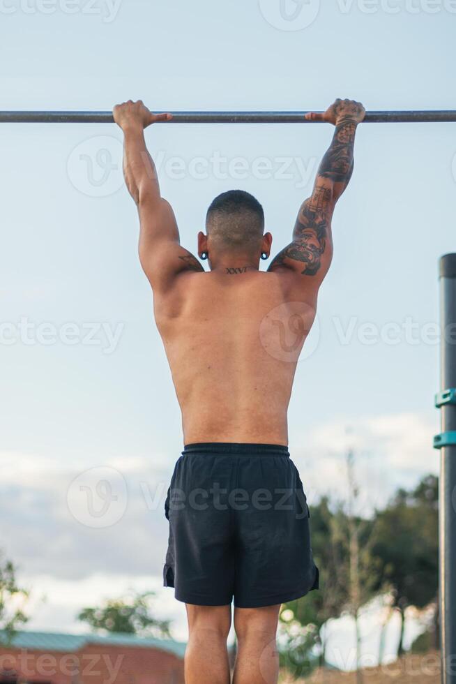 back view of a male athlete doing pull ups on a bar outdoors. calisthenics photo