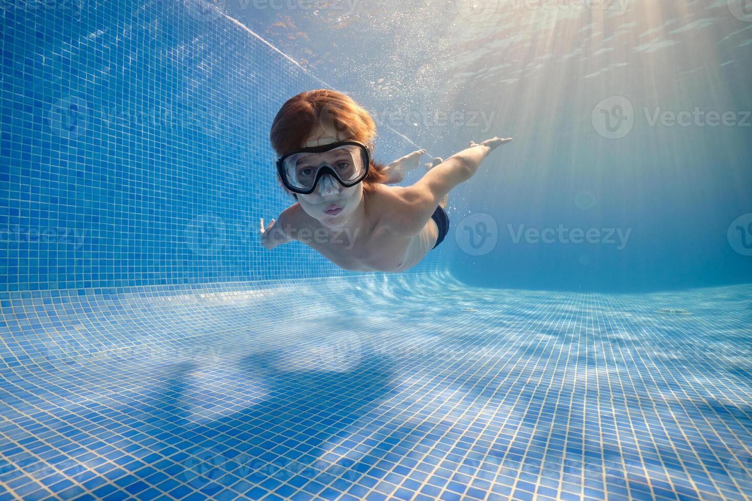 Small boy in mask swimming underwater of pool photo