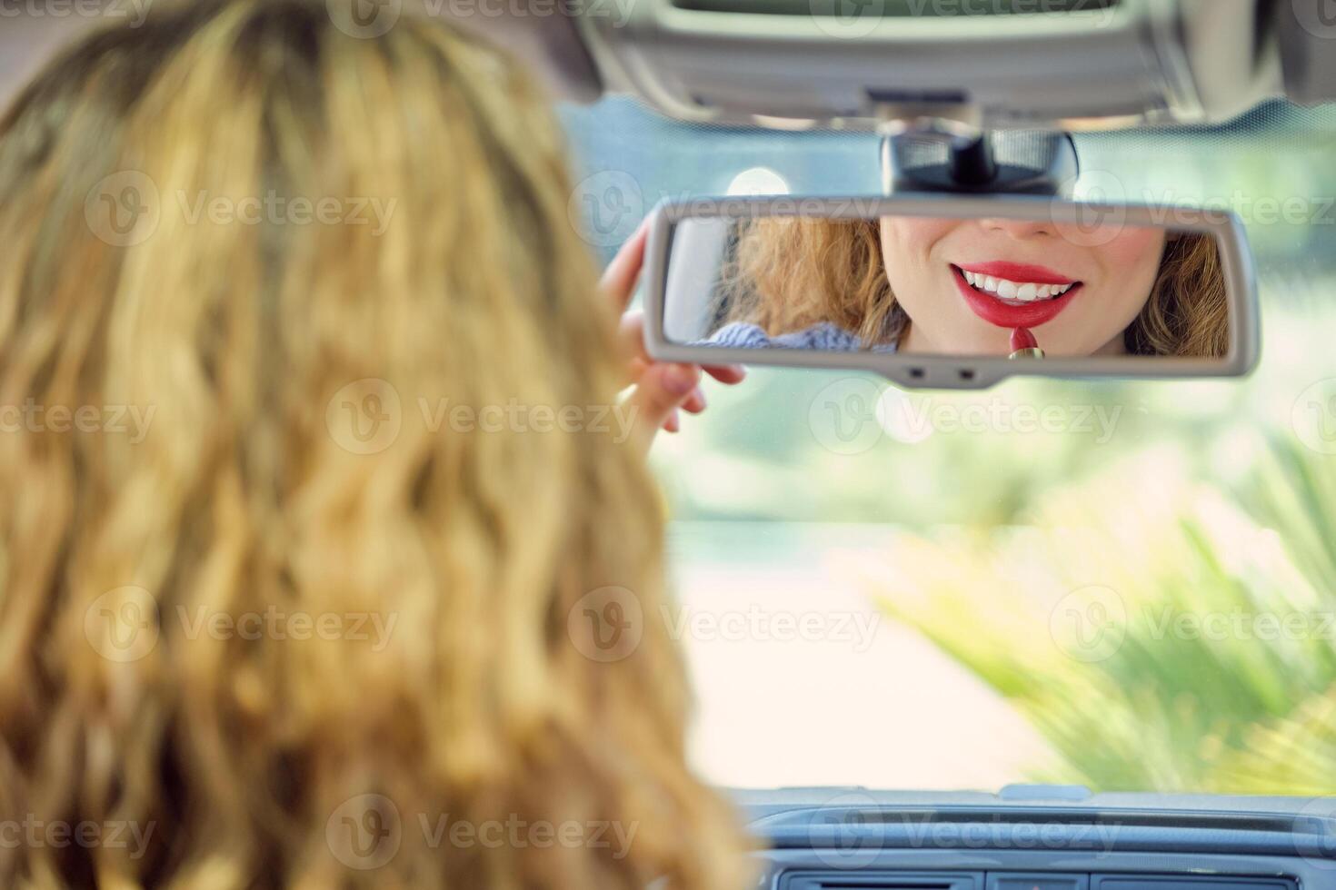 Smiling woman applying red lipstick in car front seat photo