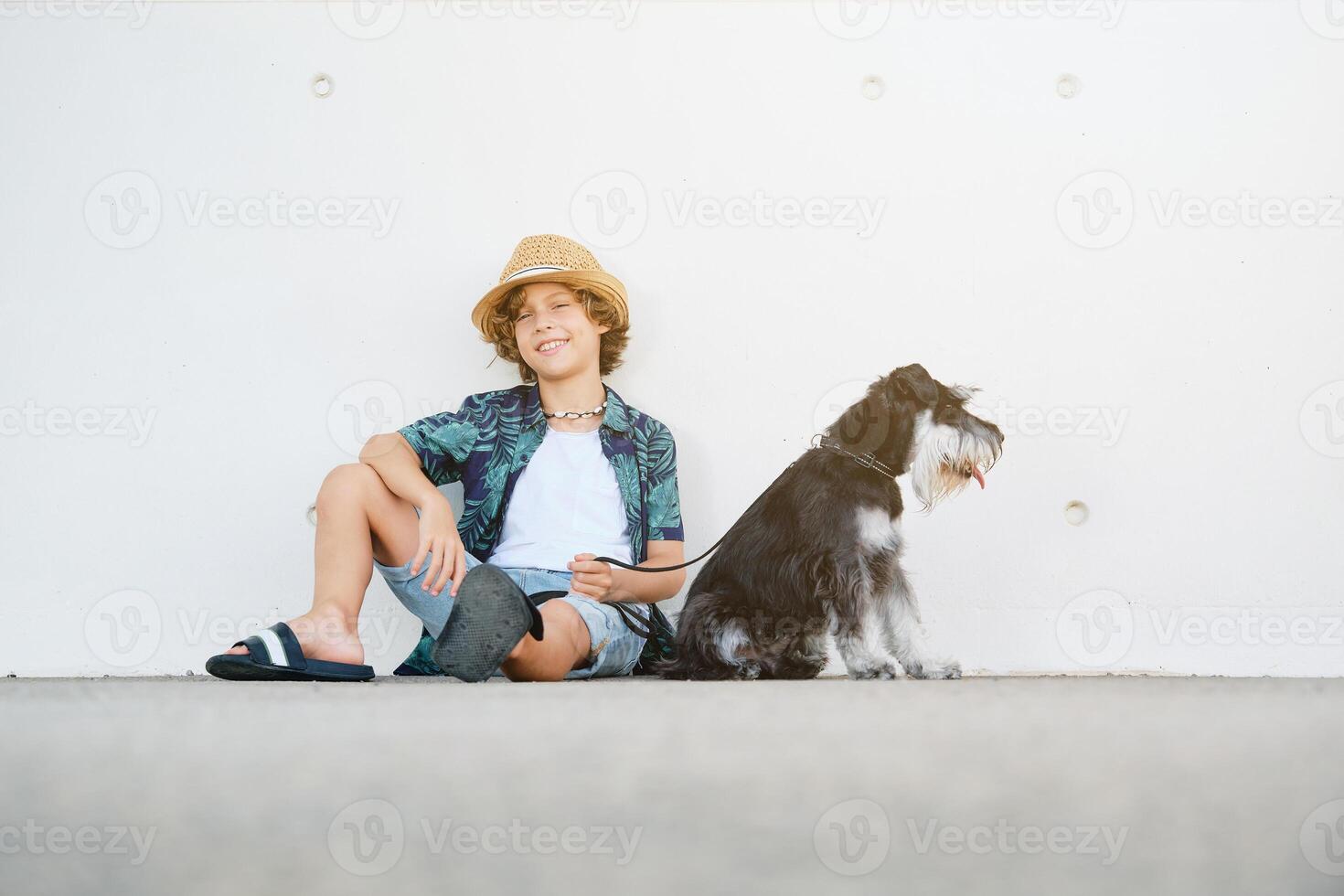 Smiling child with dog sitting against wall photo