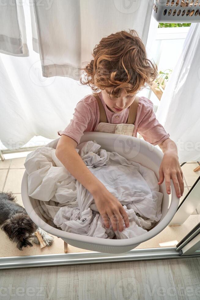 Boy taking sheets from laundry basin on balcony photo