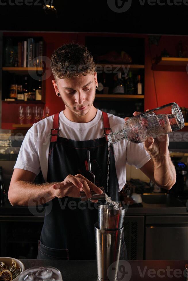 Male barkeeper pouring vodka and syrup into cobbler shaker photo
