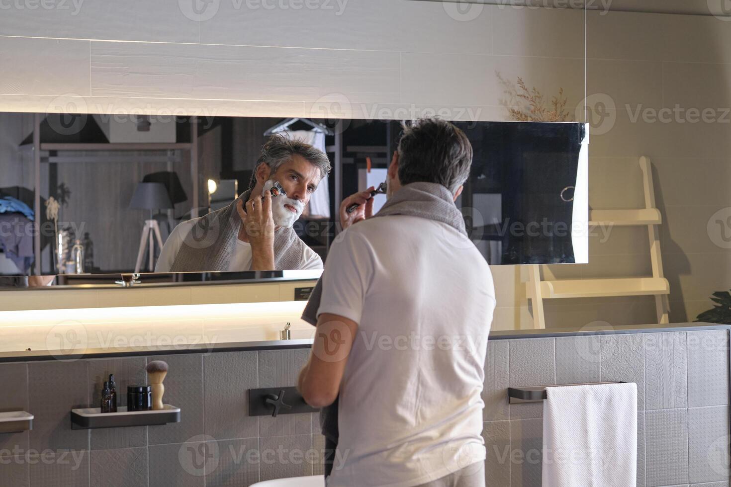 Adult male looking at mirror and shaving using razor photo