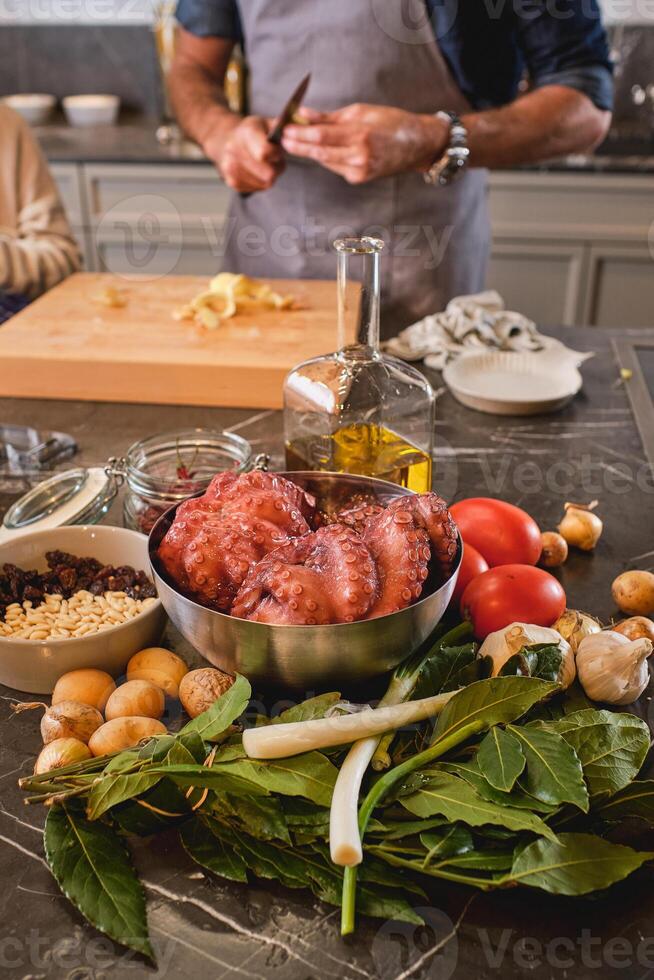 Unrecognizable man peeling vegetables at table with raw octopus photo