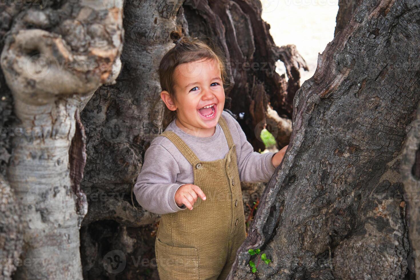 Joyful little girl standing near old tree trunk photo