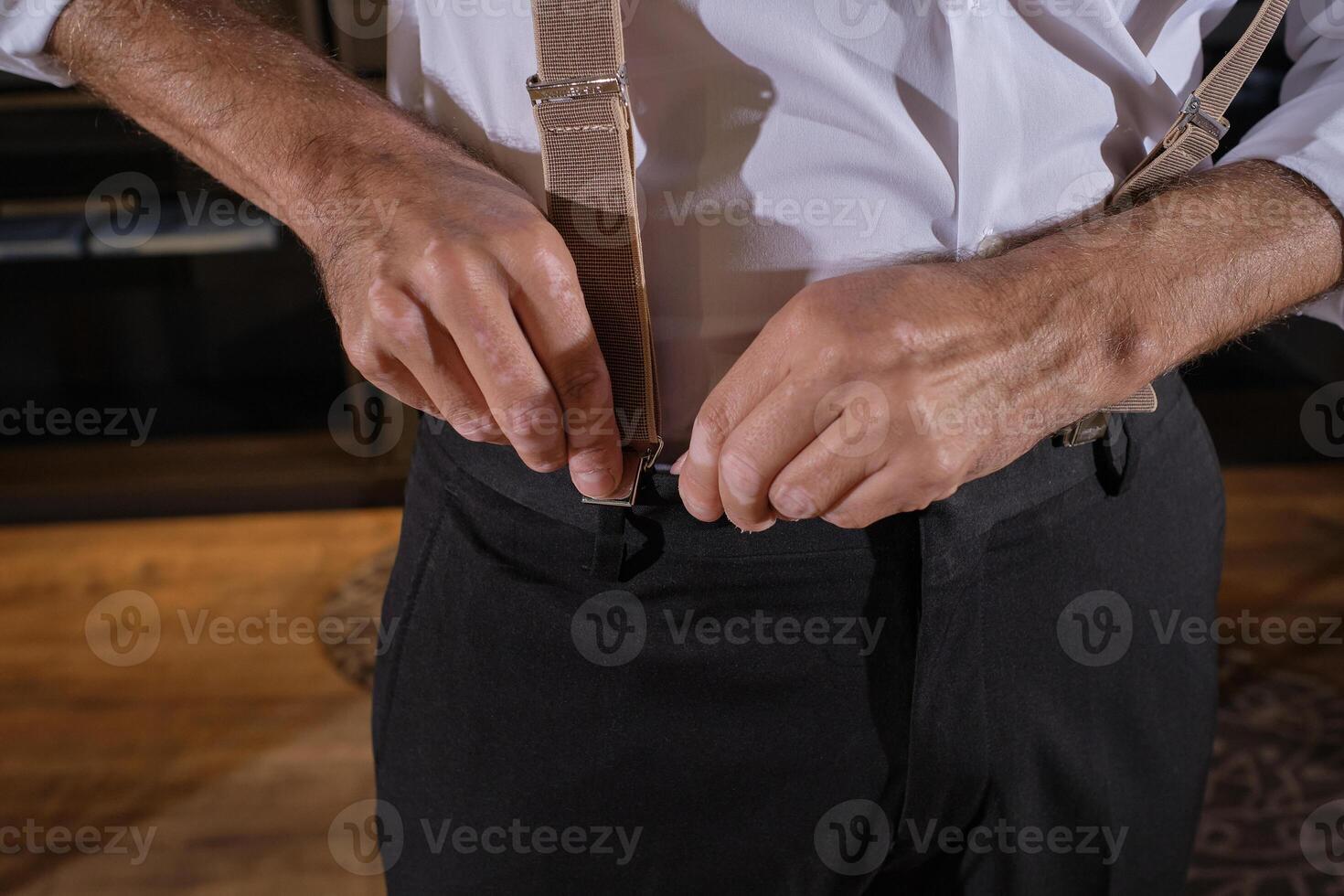 Crop man putting on suspenders for trousers in dressing room photo