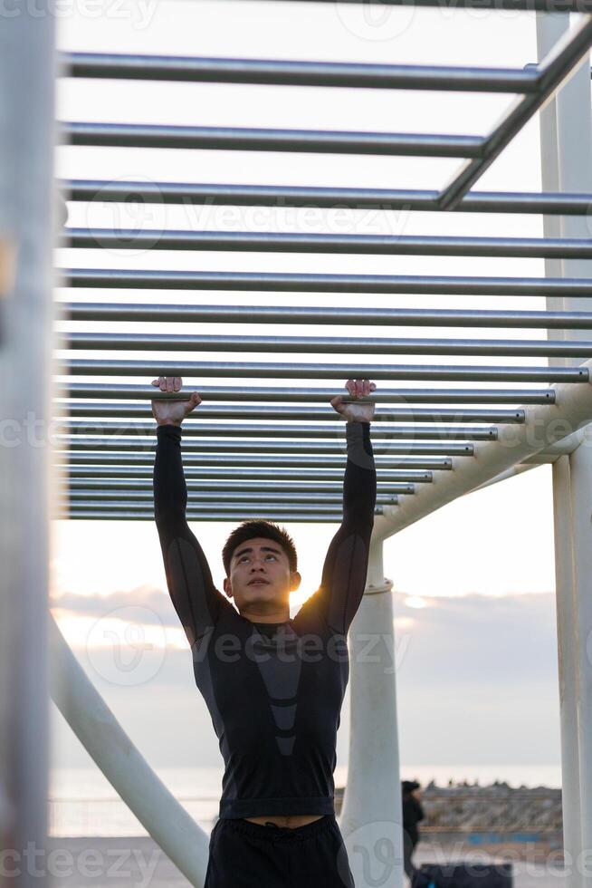 Ethnic sportsman exercising on monkey bars. Young man in action photo