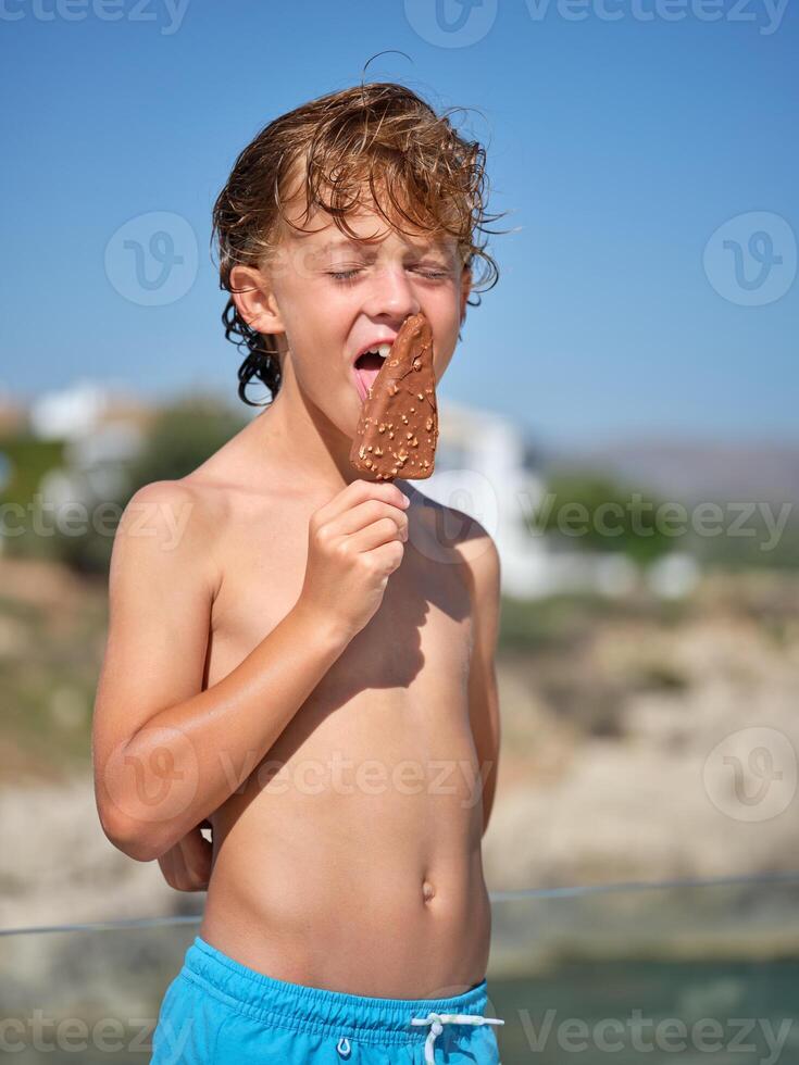 Happy boy licking ice cream while standing on beach photo