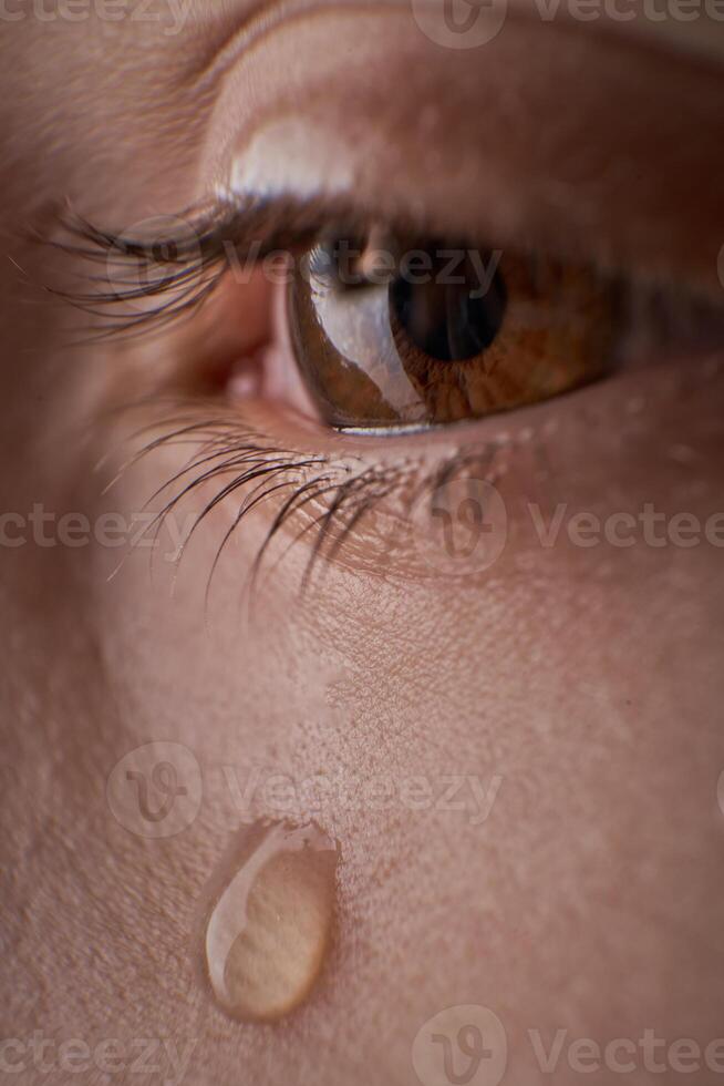 Eye of unrecognizable discontent kid with tear photo
