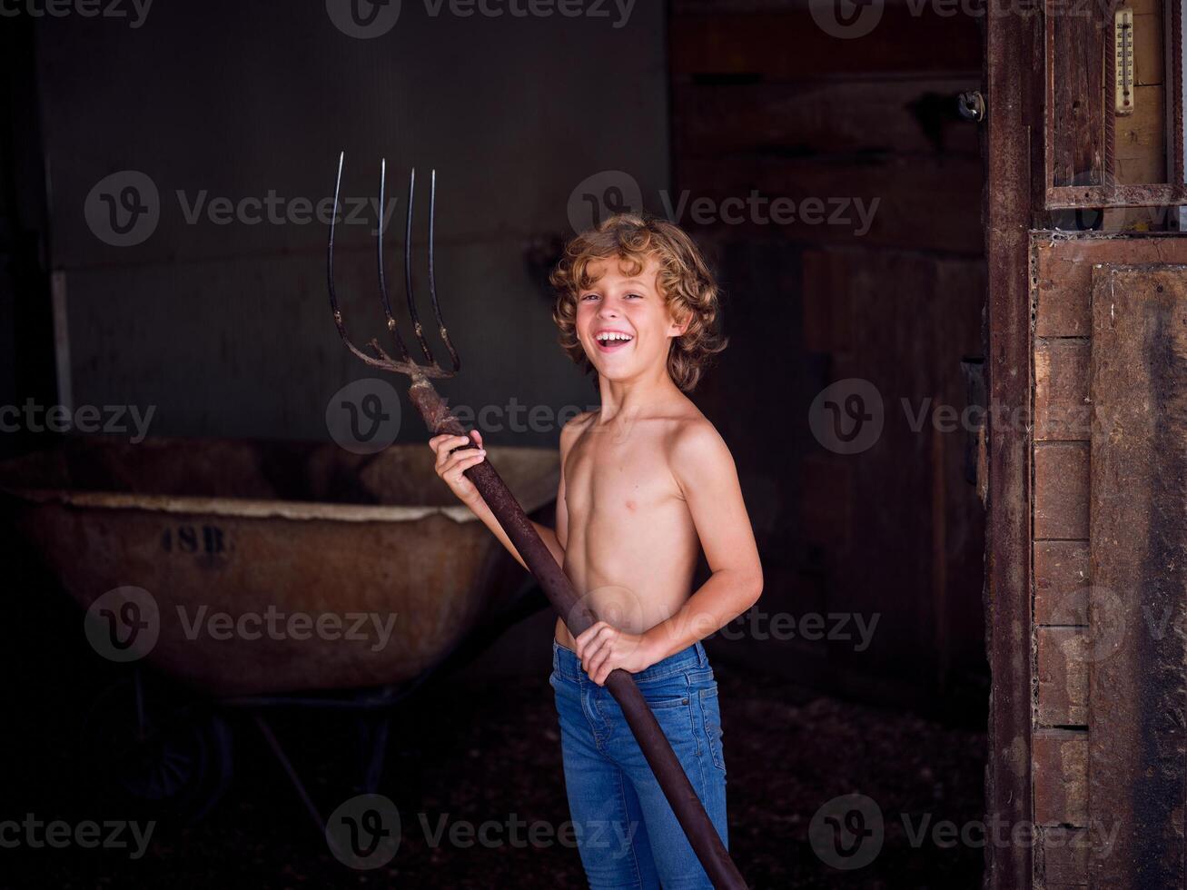 Cheerful kid with pitchfork standing in barn photo