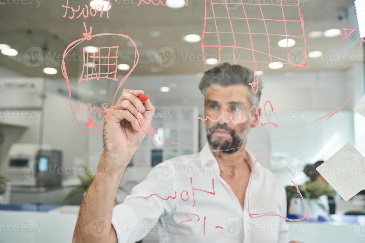 Serious bearded man working and writing on glass wall photo