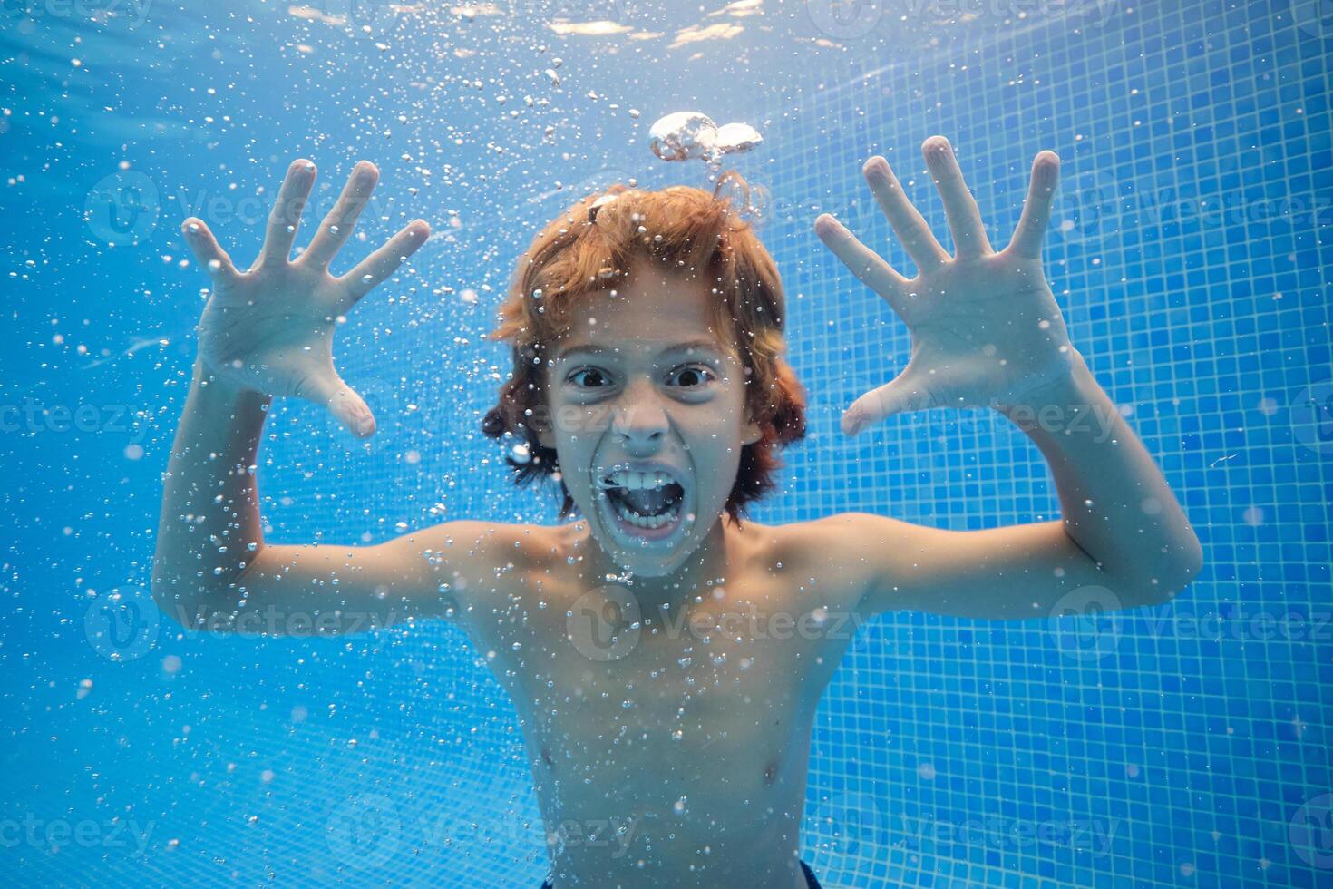 Crazy boy making grimace underwater of swimming pool photo