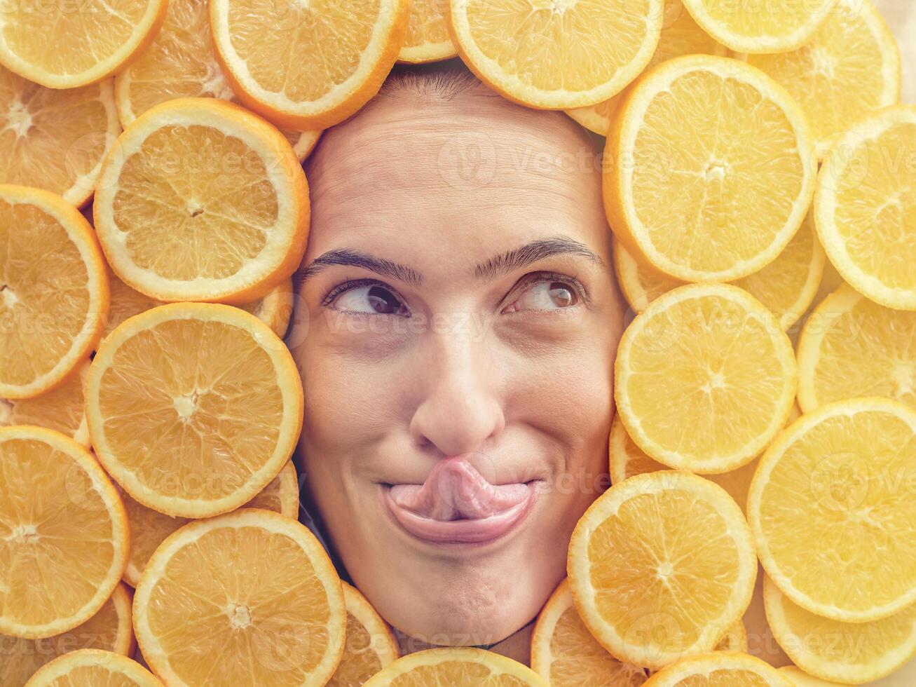 Funny woman licking nose among slices of oranges photo