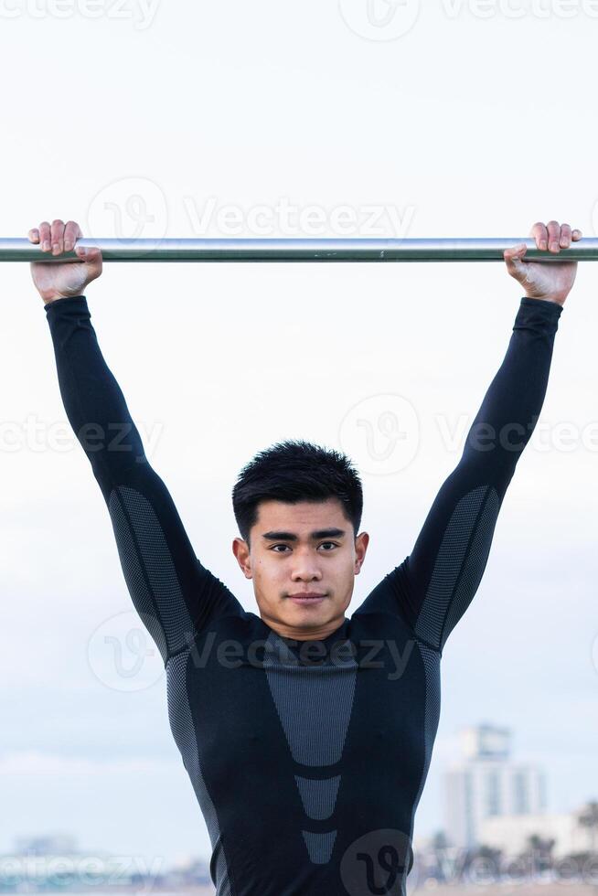 Ethnic sportsman exercising on monkey bars. photo