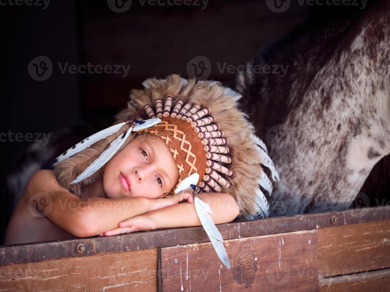 Dreamy kid in roach leaning on horse stable enclosure photo