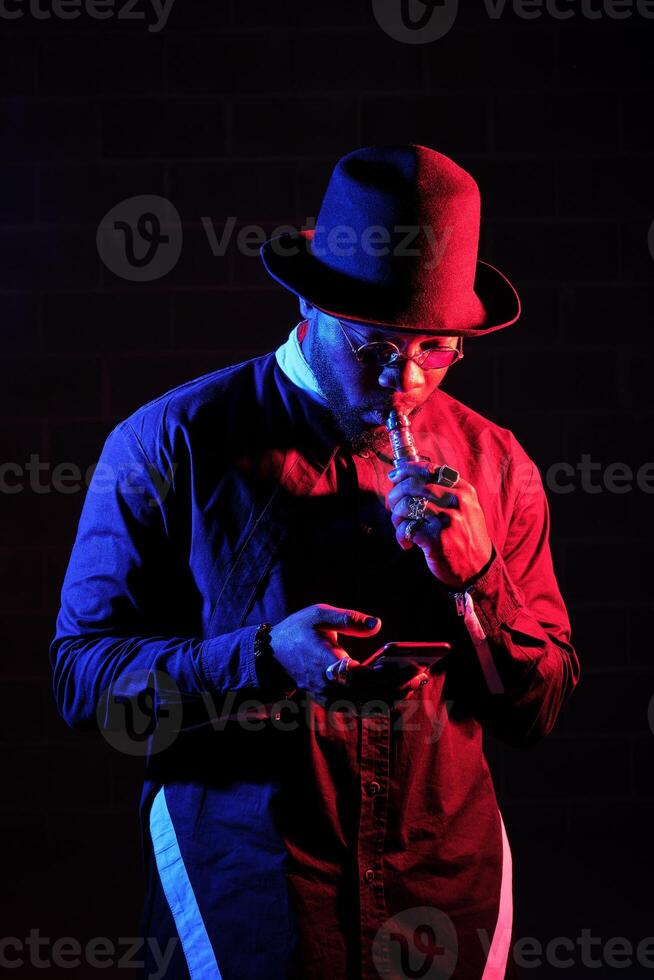 Stylish African American man vaping and browsing smartphone photo