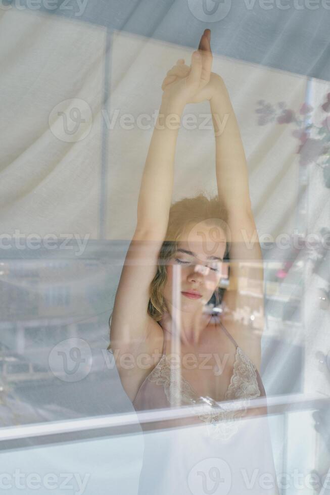 Serene woman stretching in morning near window photo