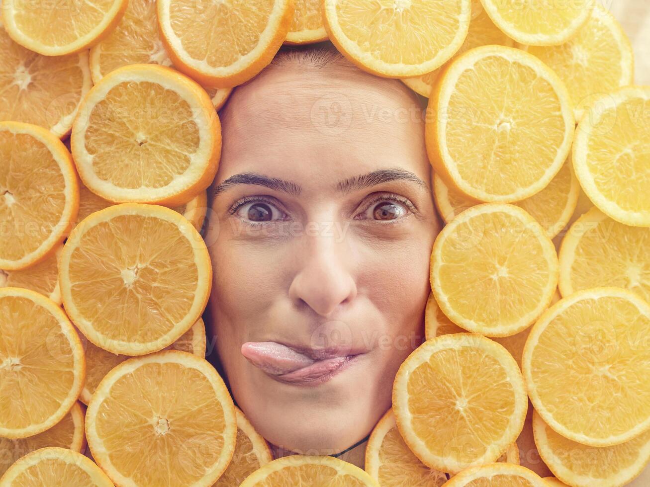 Funny woman covered in orange slices showing tongue photo