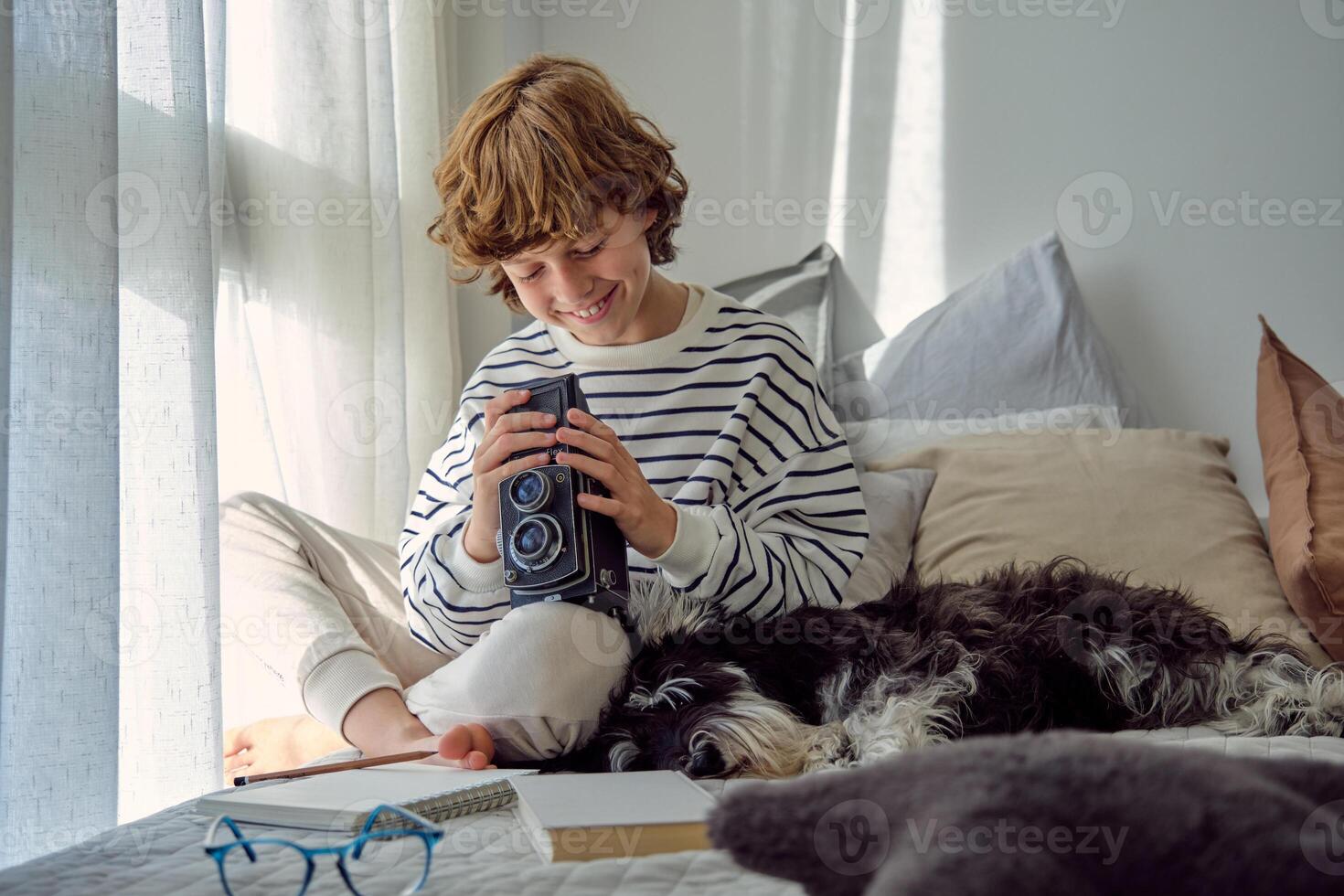 Smiling schoolboy with aged photo camera and dog on bed